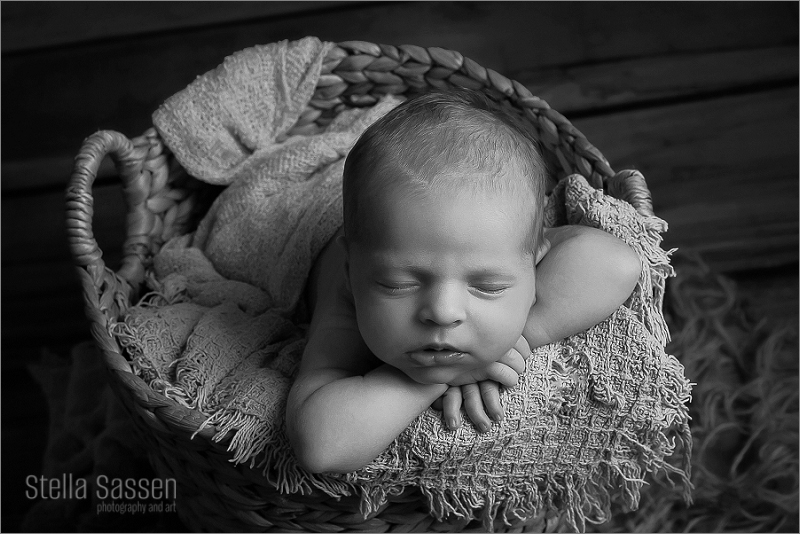 Newborn baby girl posing in basket sleeping during photo shoot