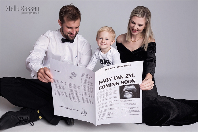 parents and toddler sitting on studio floor reading pregnancy announcement