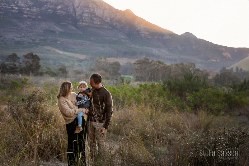 Family standing in field with baby boy with sun setting behind the mountain