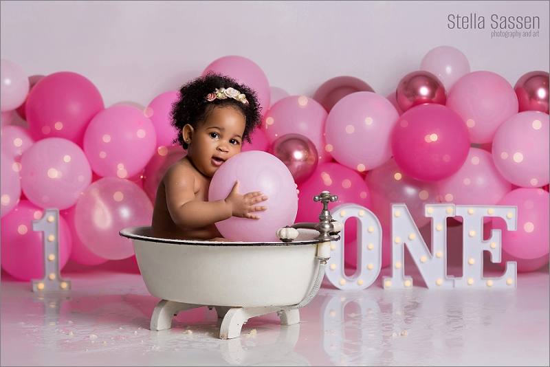 baby sitting in bath during cake smash shoot with a pink balloon and twinkly light theme