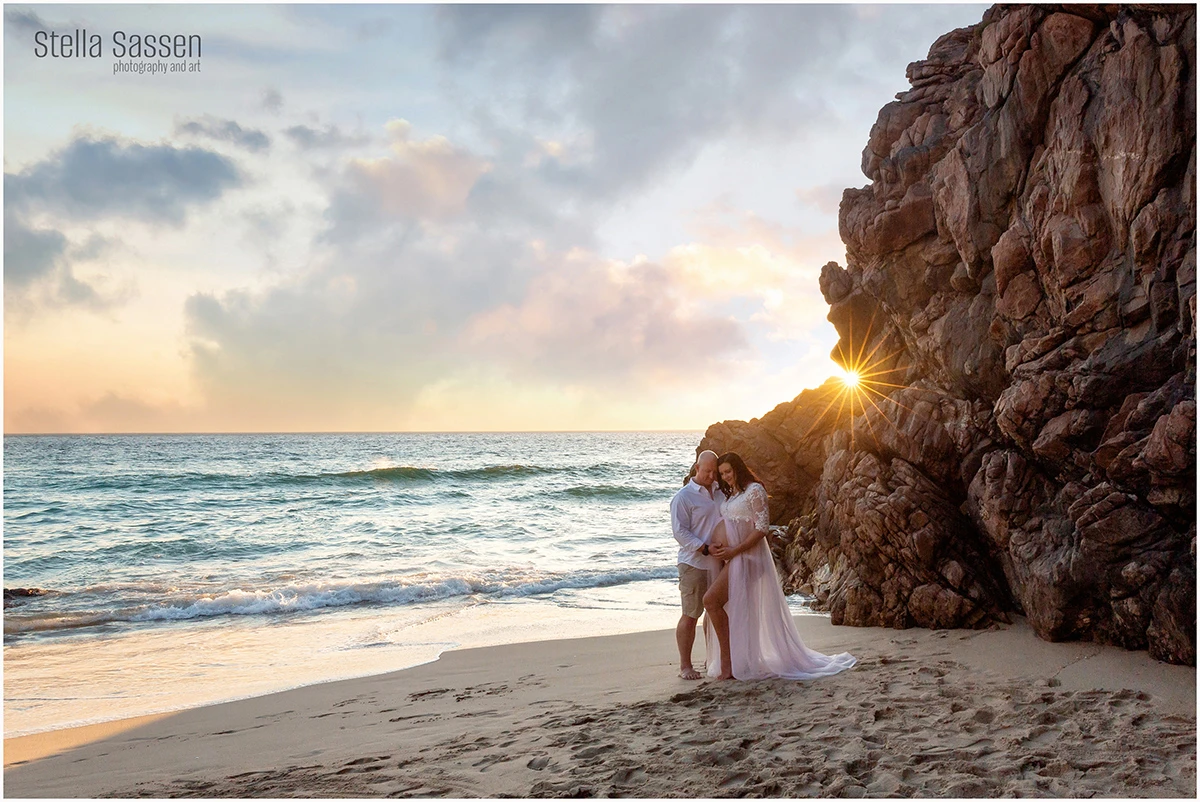 Maternity photo shoot on beach with beach and rocks in the background at sunset