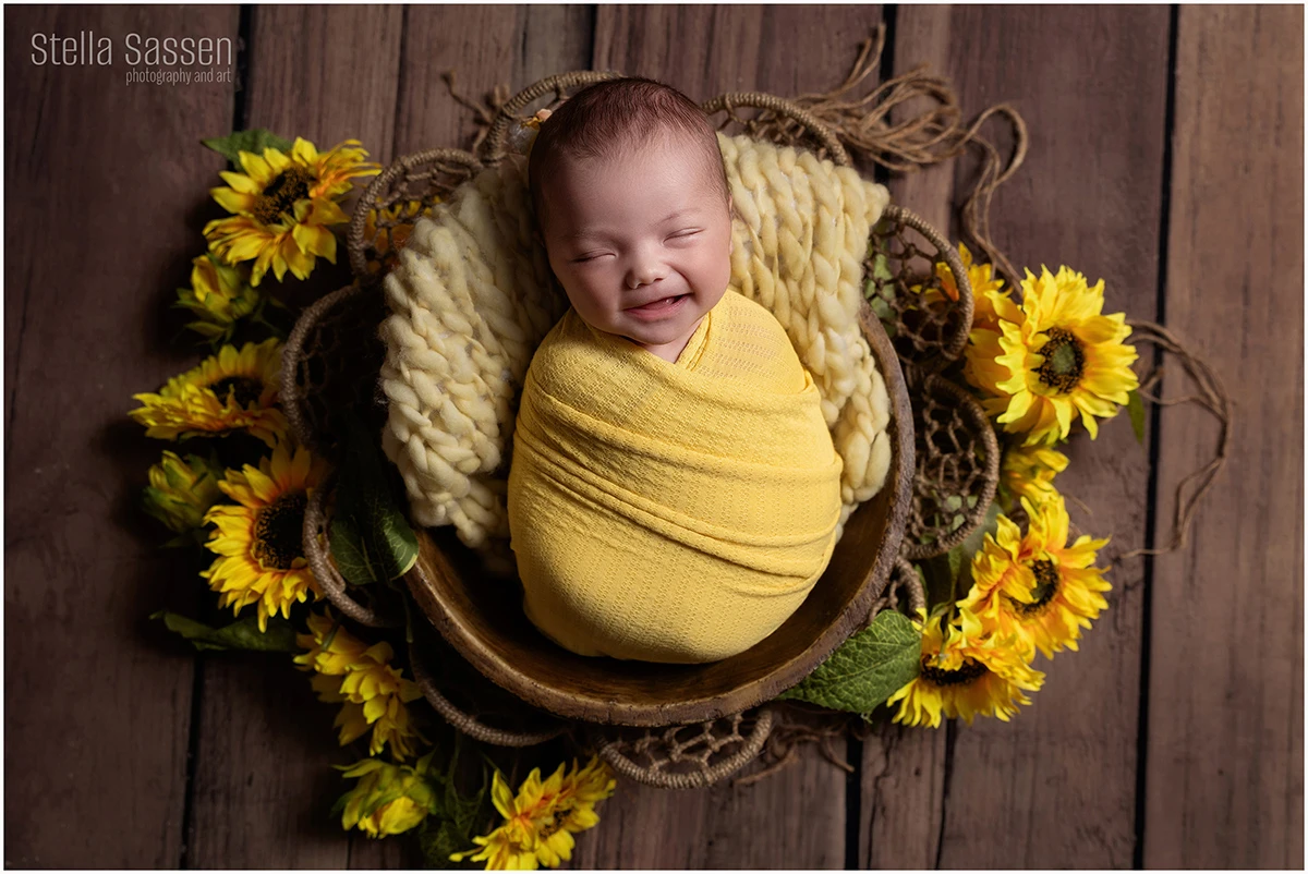 newborn baby in prop with yellow sunflowers smiling