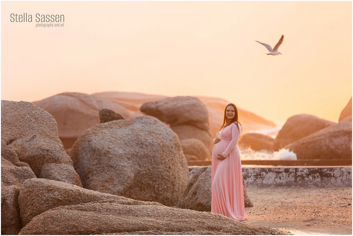 Pregnant woman during maternity photo shoot on beach at sunset with gull flying in the background