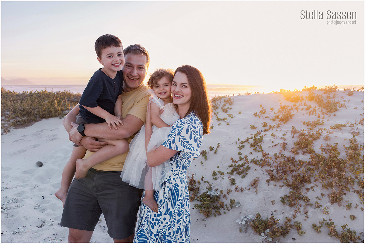 a family posed on Blouberg Beach as the sun sets over the sea